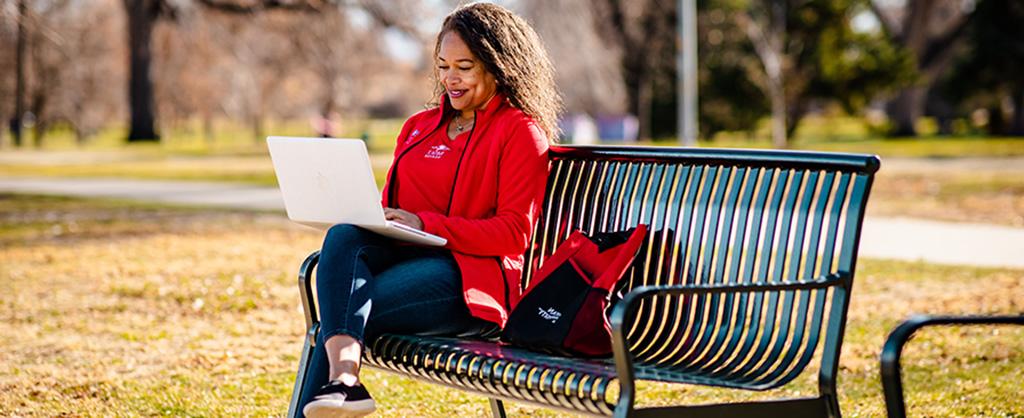 Woman in MSU Denver clothing sitting on a bench with her computer