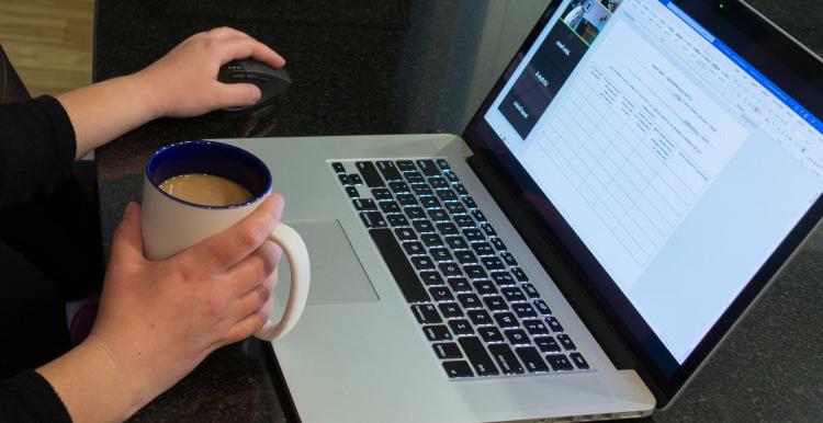 A close up of a woman holding coffee while working on her laptop.