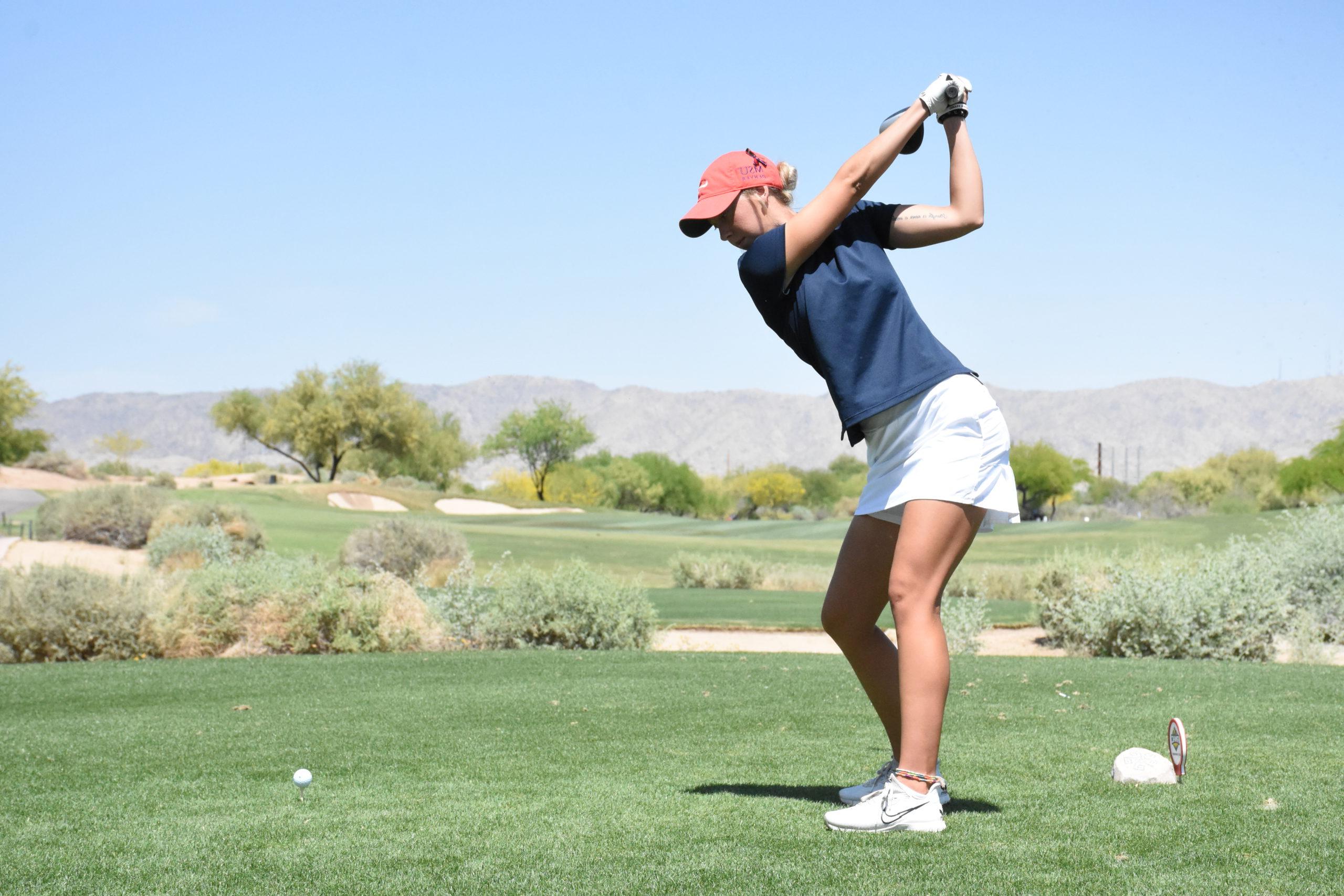 高尔夫运动员考特尼·劳勒(Courtney Lawler)在沙漠高尔夫球场开球，面前是山脉和树木.