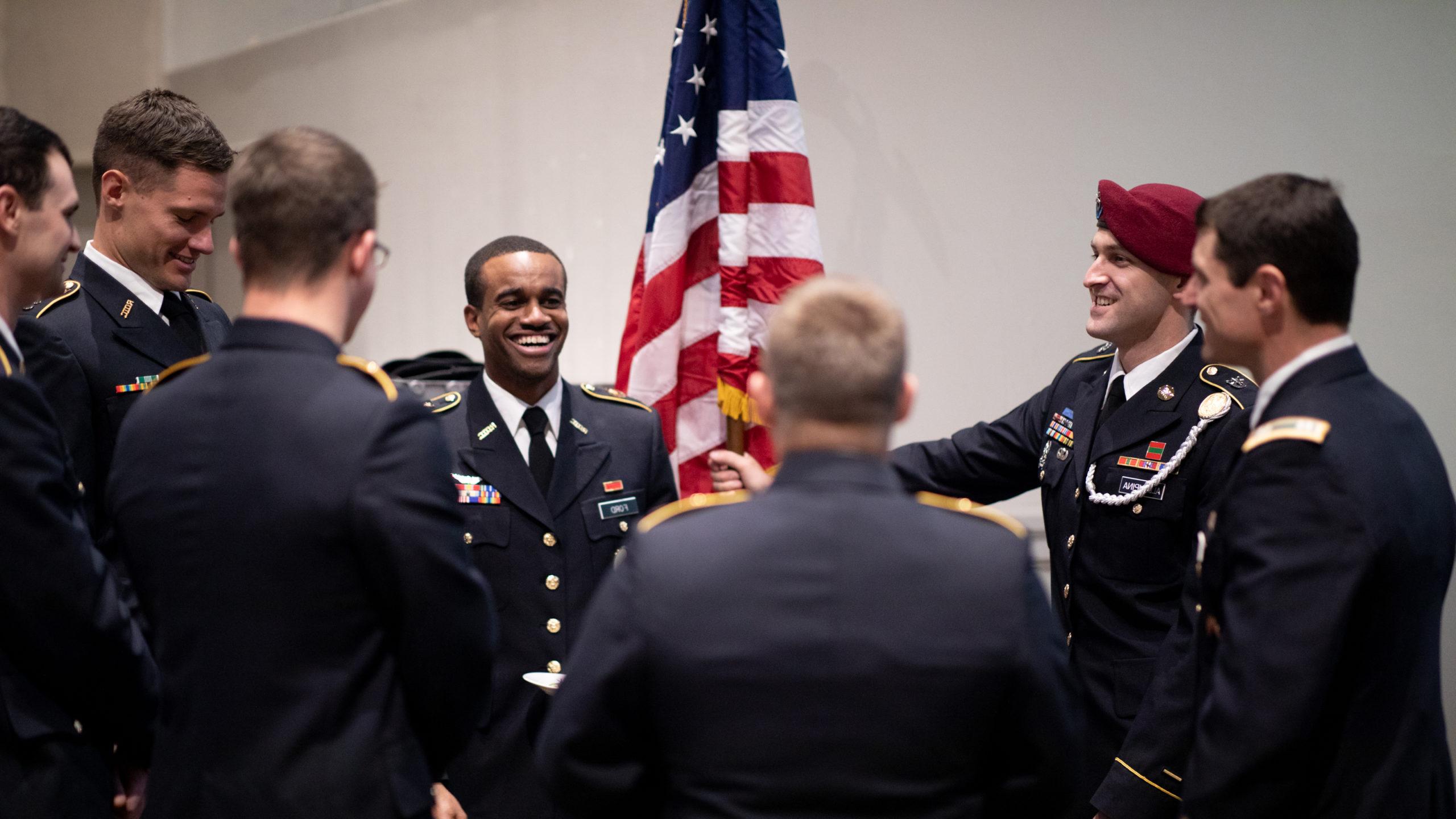 Veteran's Graduation, graduates dressed in military uniforms laughing in front of an American flag