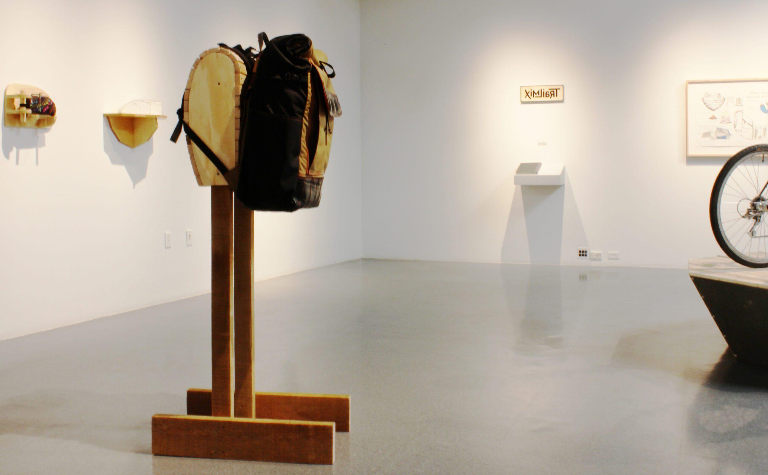 Gallery space with tall ceilings, handmade backpack on a wooden display.