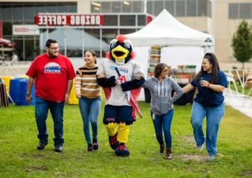 Four alumns walking with Rowdy the Roadrunner at the Homecoming Tailgate on the grass outside of the JSSB building