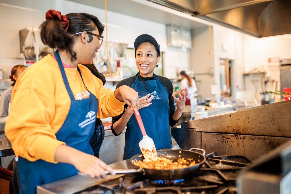 Two smiling female students cooking in a pan